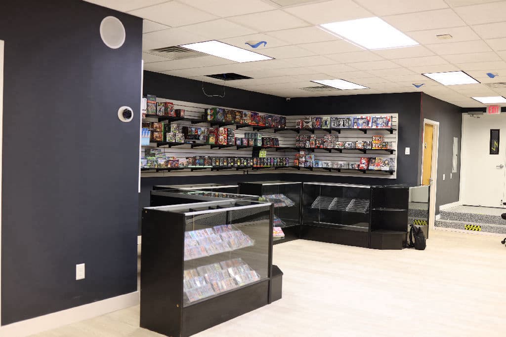 Corner of The Card Collective NY with slatwall shelving of sealed booster boxes, tins and collector sets